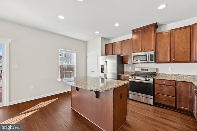 kitchen featuring a kitchen island, appliances with stainless steel finishes, a kitchen bar, dark hardwood / wood-style floors, and light stone countertops