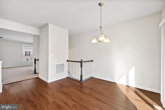 empty room featuring wood-type flooring and a notable chandelier