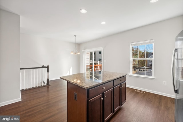 kitchen featuring hanging light fixtures, a kitchen island, light stone counters, and dark hardwood / wood-style flooring