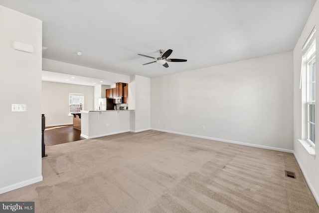 unfurnished living room with light colored carpet and ceiling fan