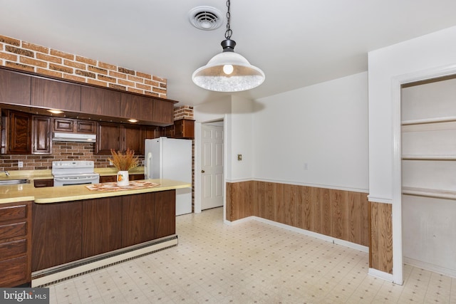 kitchen featuring dark brown cabinetry, wood walls, backsplash, pendant lighting, and white appliances