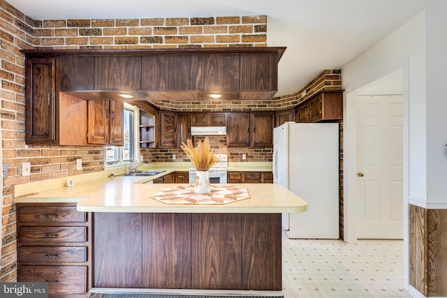 kitchen featuring kitchen peninsula, dark brown cabinetry, sink, and white appliances