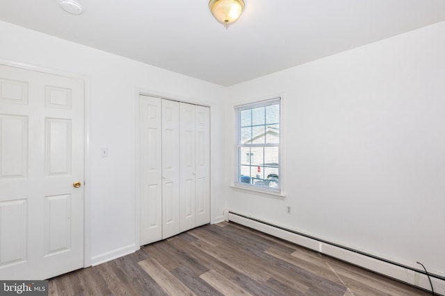 unfurnished bedroom featuring a closet, wood-type flooring, and a baseboard heating unit