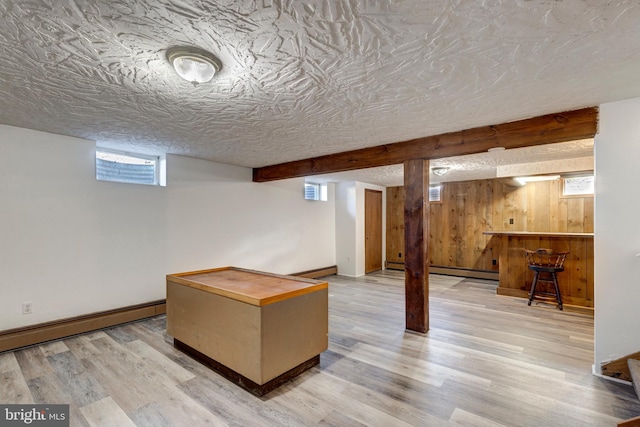 basement featuring plenty of natural light, light wood-type flooring, and a baseboard radiator