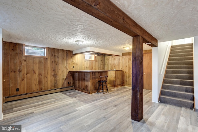 bar featuring wooden walls, light wood-type flooring, a baseboard heating unit, and a textured ceiling