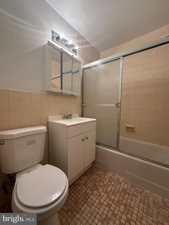 full bathroom with vanity, bath / shower combo with glass door, tile walls, and toilet