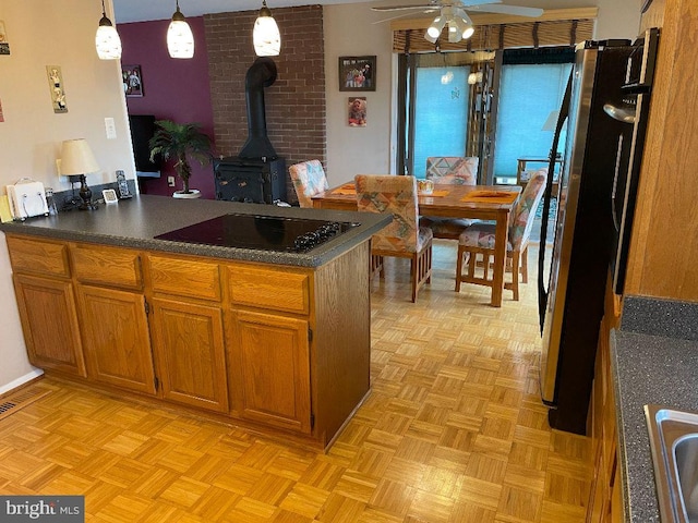 kitchen featuring stainless steel fridge, ceiling fan, a wood stove, decorative light fixtures, and black stovetop