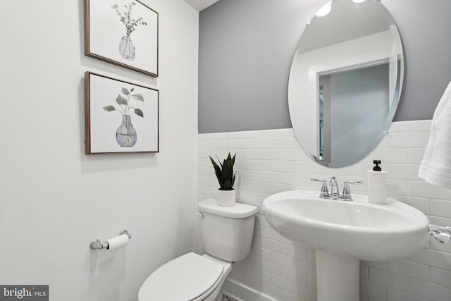 bathroom featuring toilet, tile walls, and sink