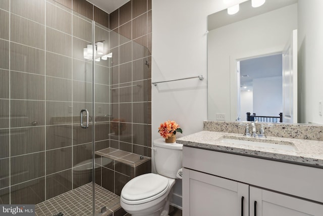 bathroom featuring a shower with door, vanity, and toilet