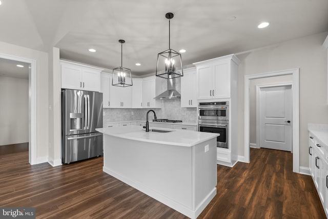 kitchen with wall chimney exhaust hood, dark wood-type flooring, stainless steel appliances, a center island with sink, and decorative light fixtures