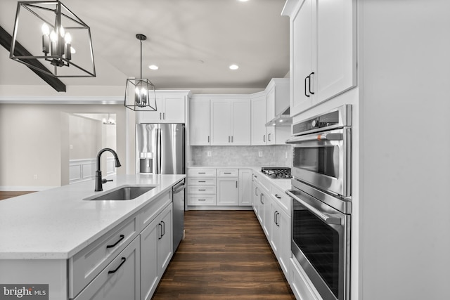 kitchen with white cabinets, an island with sink, appliances with stainless steel finishes, dark wood-type flooring, and wall chimney exhaust hood