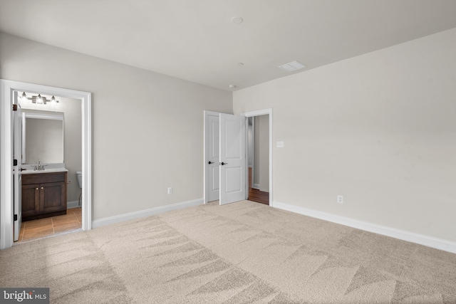 unfurnished bedroom with light colored carpet, connected bathroom, and sink