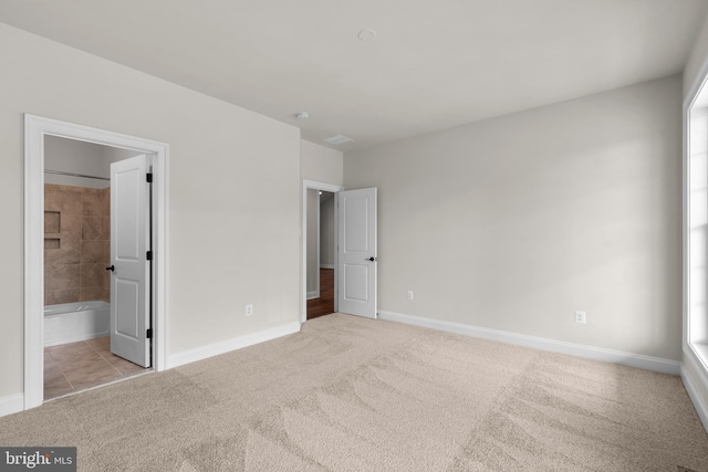 unfurnished bedroom featuring light carpet and ensuite bath