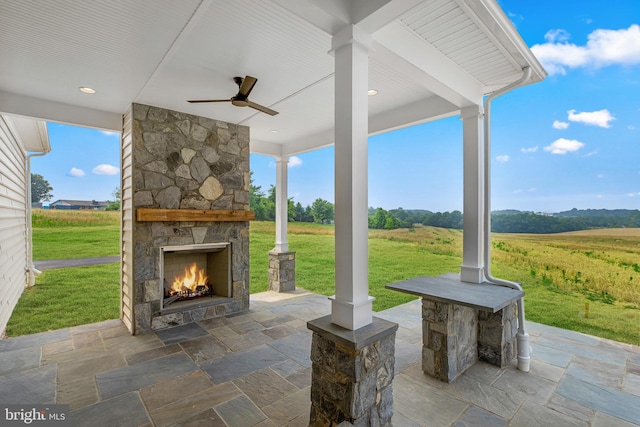 view of patio with a rural view, an outdoor stone fireplace, and ceiling fan