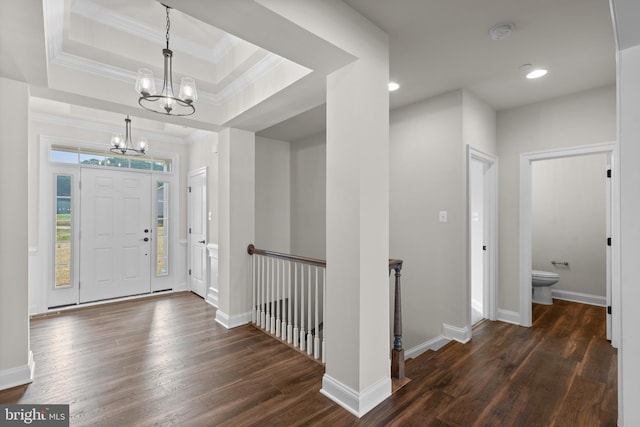 entryway featuring crown molding, a raised ceiling, a notable chandelier, and dark hardwood / wood-style flooring