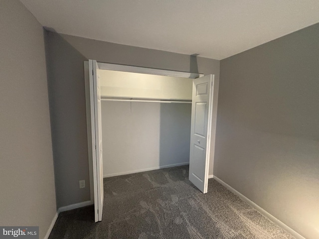 unfurnished bedroom with dark colored carpet and a closet