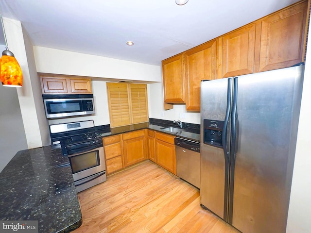 kitchen featuring sink, appliances with stainless steel finishes, dark stone countertops, decorative light fixtures, and light hardwood / wood-style flooring