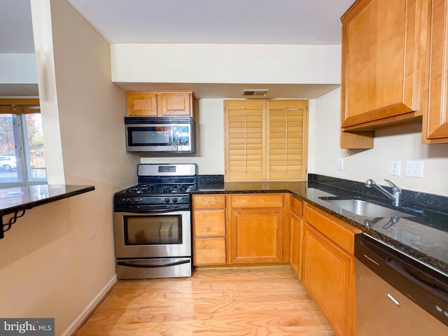 kitchen featuring stainless steel appliances, sink, dark stone countertops, and light hardwood / wood-style flooring