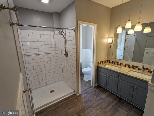 bathroom with hardwood / wood-style floors, vanity, a tile shower, and toilet