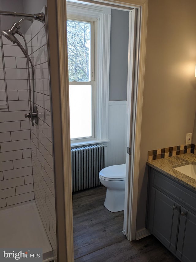 bathroom featuring radiator, vanity, tiled shower, wood-type flooring, and toilet