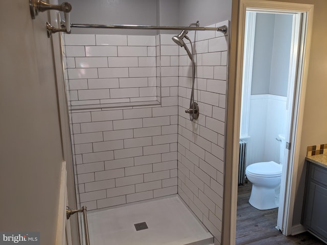 bathroom featuring vanity, tiled shower, hardwood / wood-style floors, radiator heating unit, and toilet