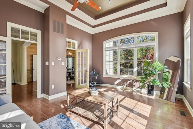 living room with light wood-type flooring, a raised ceiling, decorative columns, ceiling fan, and crown molding