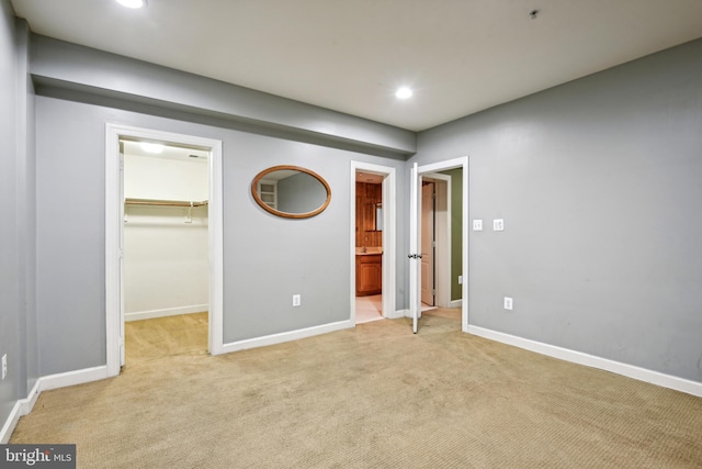 unfurnished bedroom featuring a spacious closet, connected bathroom, a closet, and light colored carpet