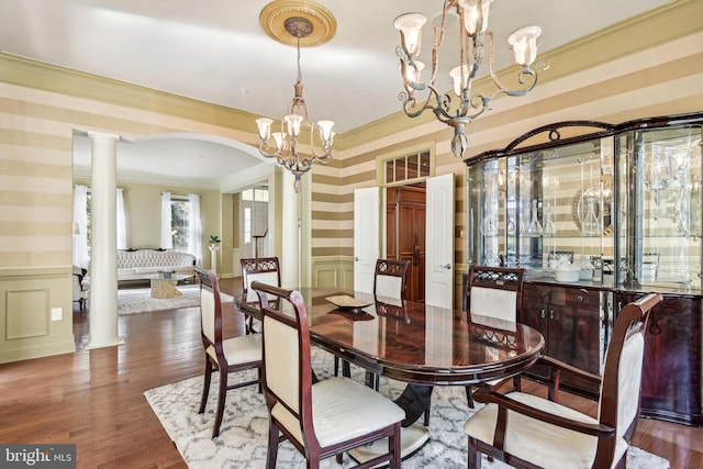 dining room with crown molding, decorative columns, wood-type flooring, and an inviting chandelier