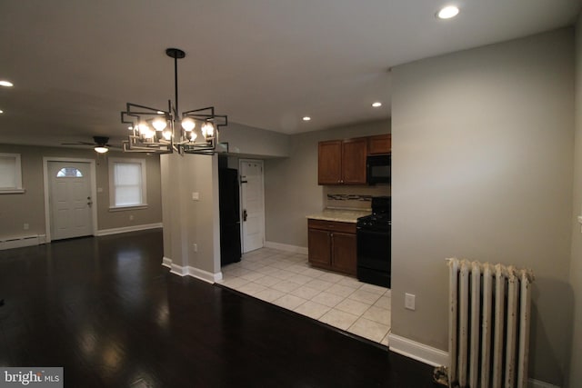 kitchen featuring radiator, pendant lighting, light tile patterned floors, black appliances, and ceiling fan with notable chandelier