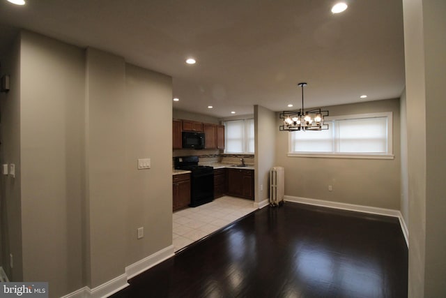 kitchen featuring radiator heating unit, sink, light hardwood / wood-style floors, decorative light fixtures, and black appliances