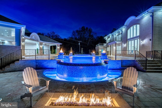 pool at night featuring a fire pit, a patio, and pool water feature