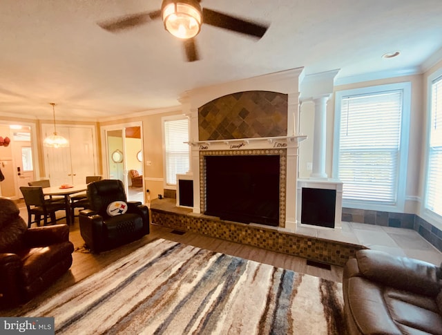 living room with hardwood / wood-style floors, crown molding, ceiling fan, a fireplace, and decorative columns