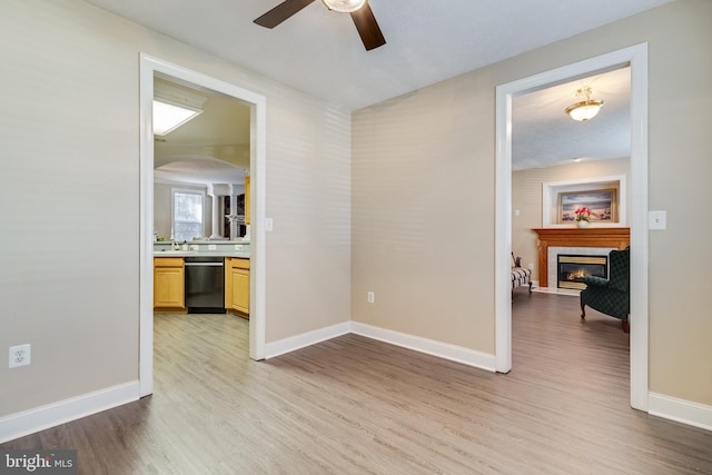 empty room with a fireplace, light hardwood / wood-style floors, ceiling fan, and sink