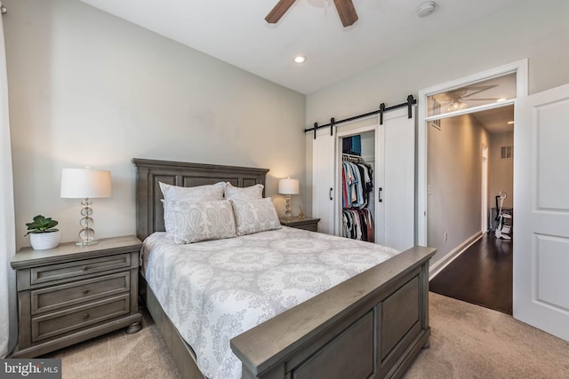 carpeted bedroom featuring a closet, ceiling fan, a walk in closet, and a barn door