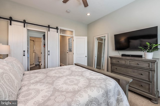 carpeted bedroom featuring a barn door, ensuite bathroom, a closet, and ceiling fan