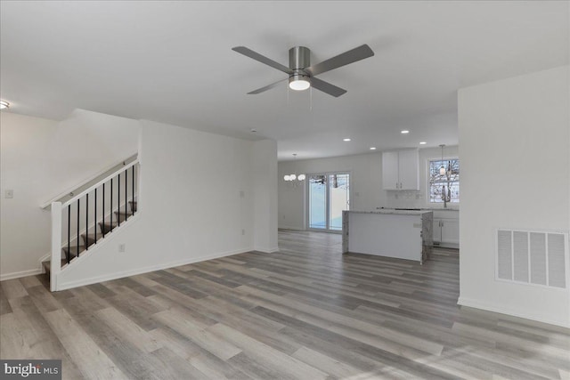 unfurnished living room featuring sink, light hardwood / wood-style floors, and ceiling fan with notable chandelier