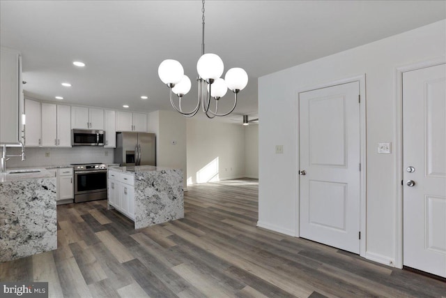 kitchen featuring hanging light fixtures, backsplash, white cabinets, light stone counters, and stainless steel appliances