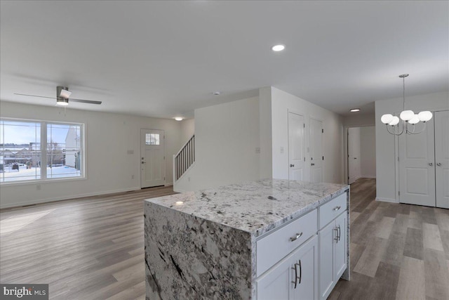 kitchen featuring white cabinets, a center island, decorative light fixtures, light wood-type flooring, and light stone counters