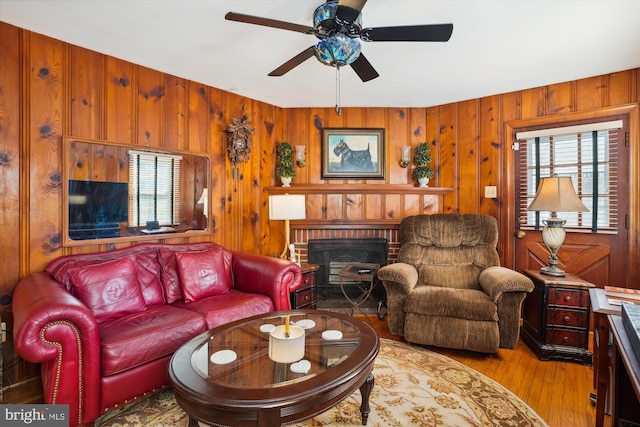 living room featuring ceiling fan, a fireplace, wooden walls, and light hardwood / wood-style flooring