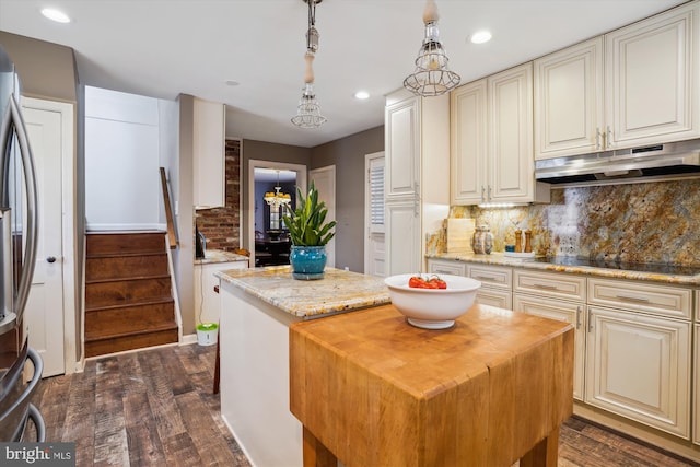 kitchen featuring light stone countertops, hanging light fixtures, dark hardwood / wood-style flooring, black electric stovetop, and a kitchen island