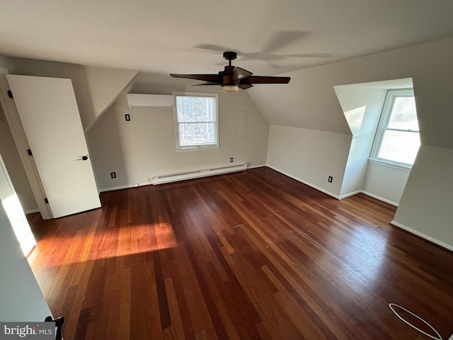 additional living space with baseboard heating, a wall mounted AC, dark hardwood / wood-style flooring, and vaulted ceiling