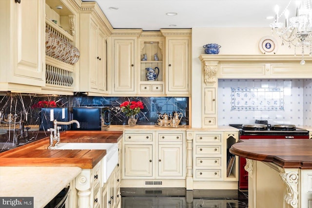 kitchen featuring cream cabinetry, tasteful backsplash, an inviting chandelier, wood counters, and pendant lighting