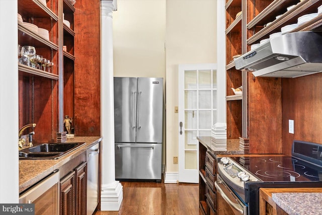 kitchen with dark hardwood / wood-style flooring, appliances with stainless steel finishes, dark stone counters, decorative columns, and sink