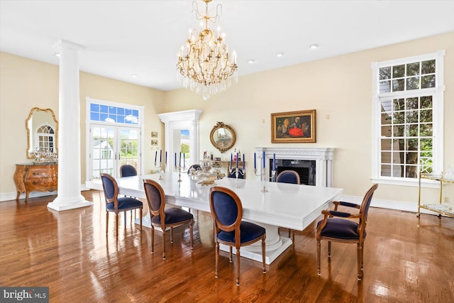 dining space with decorative columns, wood-type flooring, an inviting chandelier, and a premium fireplace