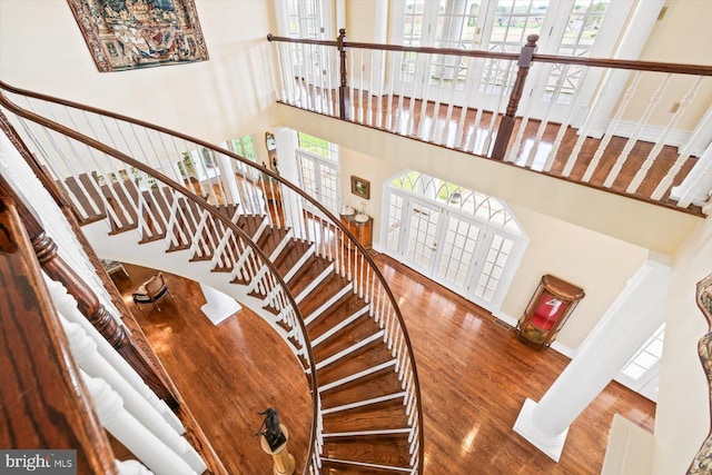 staircase with french doors, hardwood / wood-style floors, a high ceiling, and decorative columns