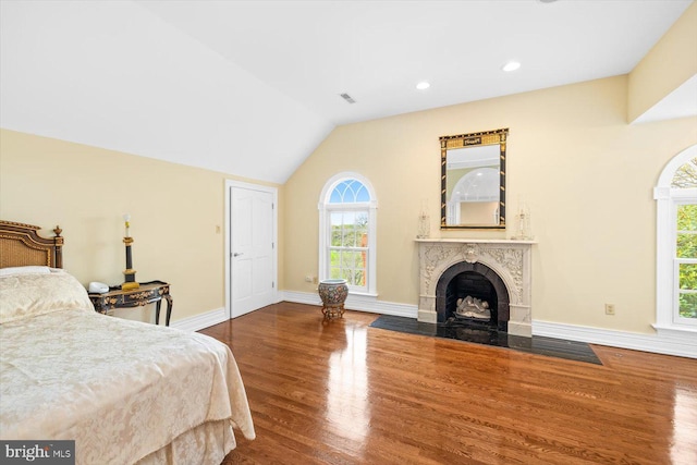 bedroom with a high end fireplace, hardwood / wood-style floors, multiple windows, and lofted ceiling