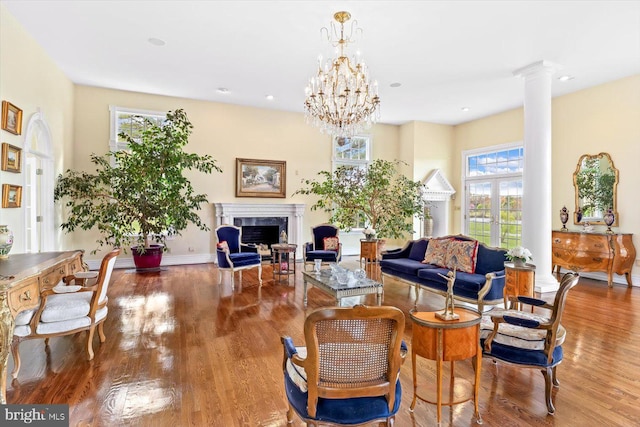 living room featuring ornate columns, hardwood / wood-style flooring, a healthy amount of sunlight, and a notable chandelier