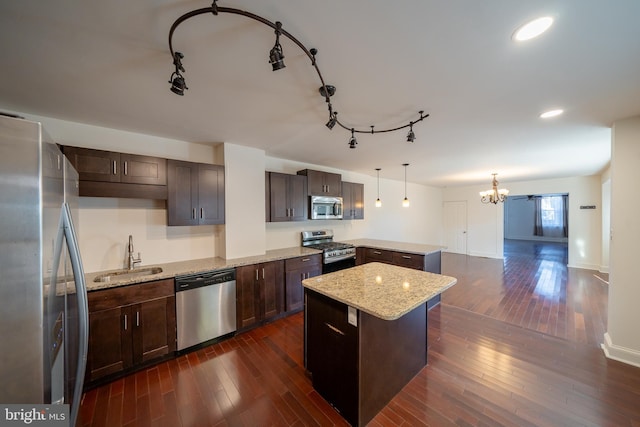 kitchen with pendant lighting, dark wood-type flooring, sink, light stone countertops, and stainless steel appliances