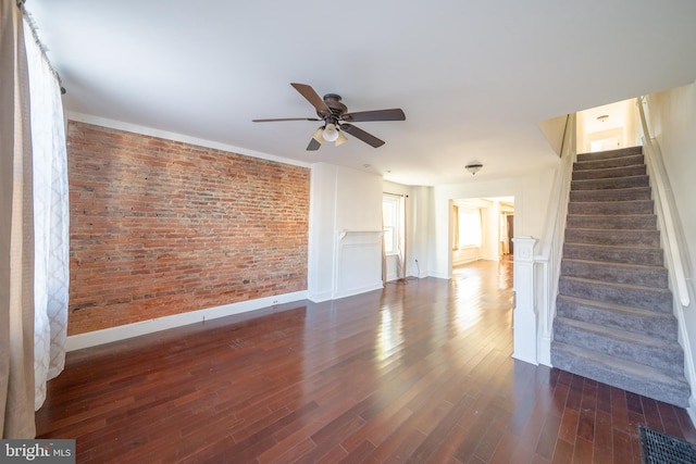 unfurnished living room featuring dark hardwood / wood-style flooring, ceiling fan, and brick wall