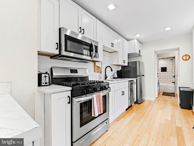 kitchen featuring stainless steel appliances, white cabinetry, sink, light hardwood / wood-style flooring, and decorative backsplash